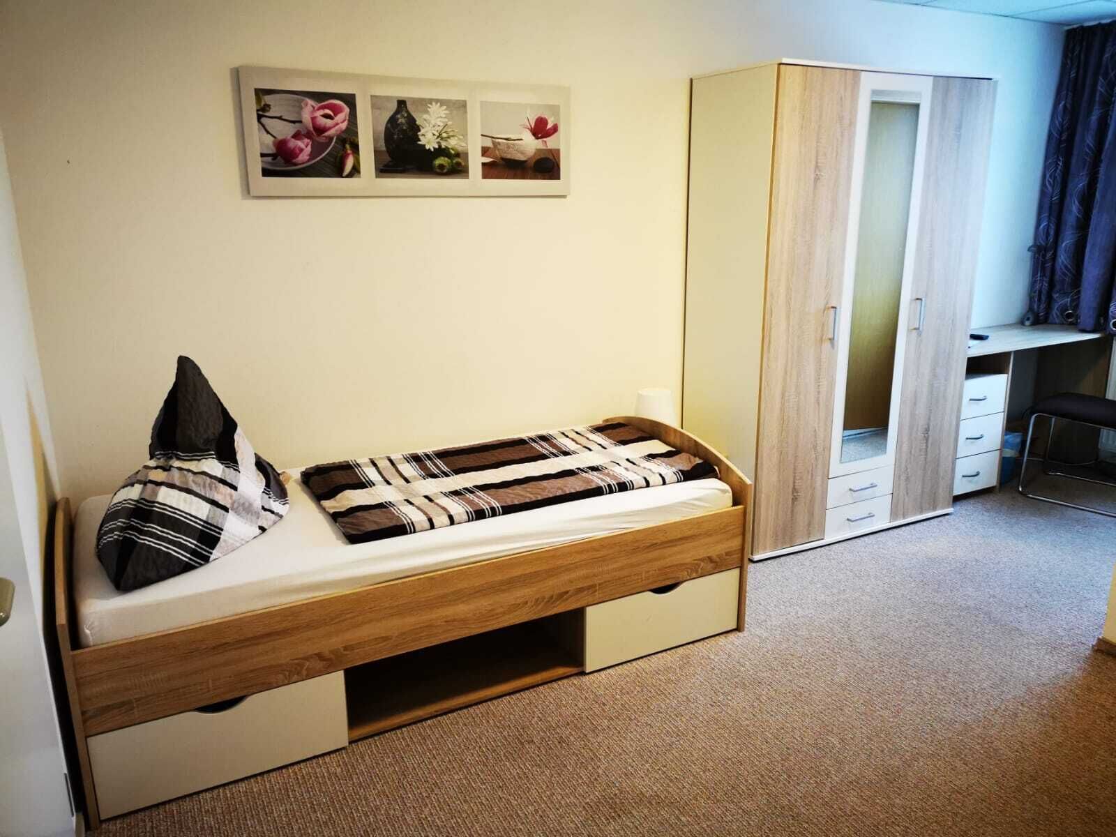 A small bedroom with a single bed, a wardrobe, and a desk.