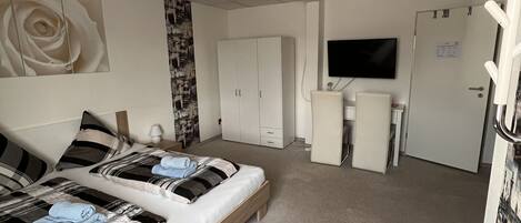 A hotel room with a large bed, a TV, a wardrobe, and a desk.