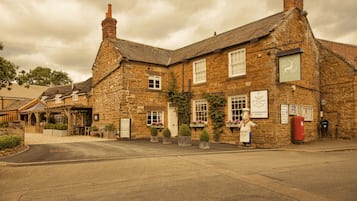 Traditional stone building with a classic pitched roof, multiple windows, and a prominent chimney, set amidst a charming garden.
