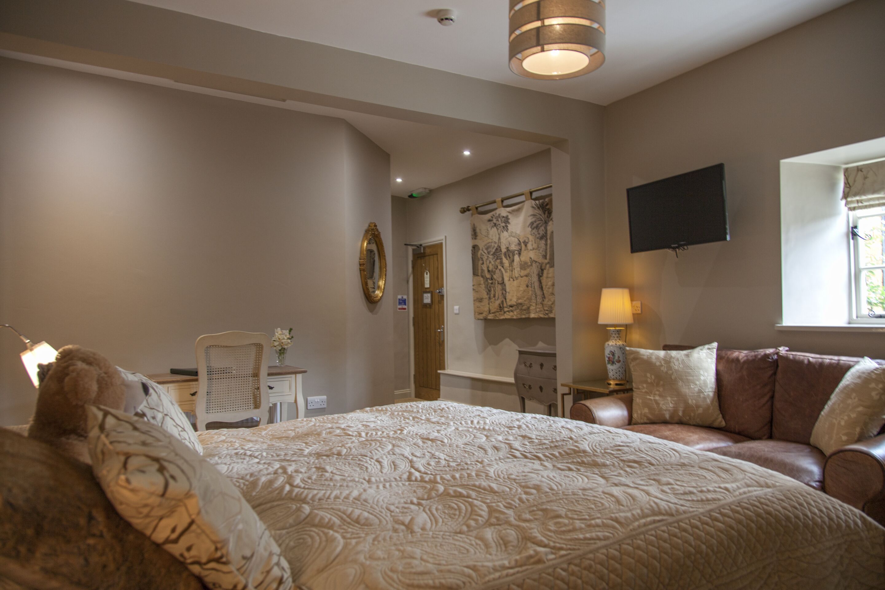 A hotel room with a large bed, a sofa, a desk, and a TV mounted on the wall.