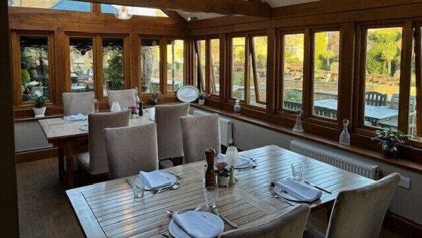 A dining area with wooden beams, large windows, and a table set for two. - Old White Hart (Oakham)