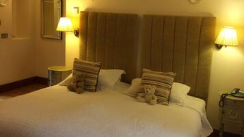 Een hotelkamer met een groot bed, twee kussens, twee bedlampjes, een nachtkastje, een spiegel en een klok aan de muur.