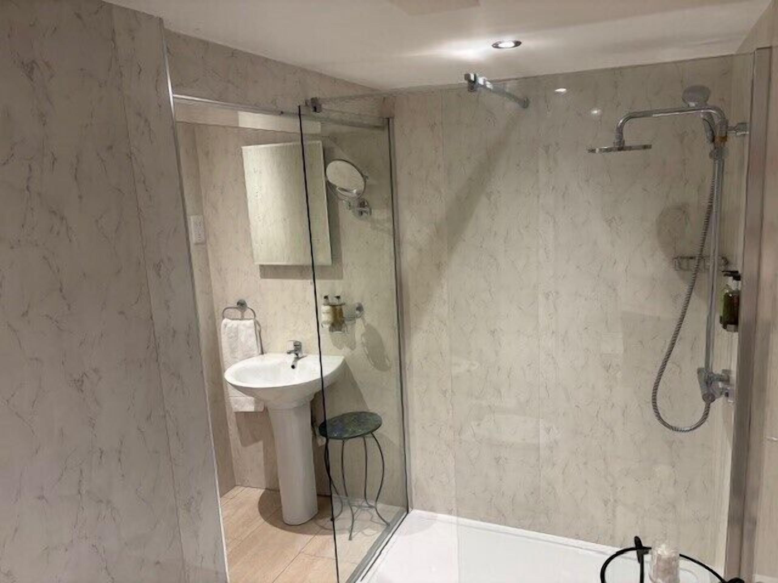 A modern bathroom with a glass-enclosed shower, a pedestal sink, and a mirror.