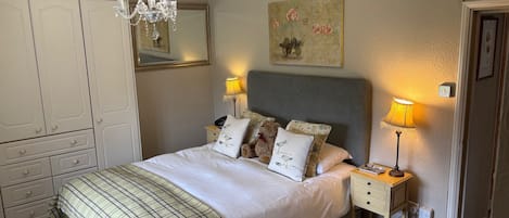 A bedroom with a bed, bedside lamps, a chandelier, a dresser, a mirror, and a painting on the wall.