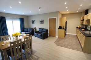A modern living room with a dining table, two black leather sofas, and a kitchen area with wooden cabinets and a black countertop. - Plawsworth Aparthotel (Chester-le-Street)