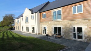 Un edificio a due piani con facciata in pietra e rivestimento in legno. Si notano diverse finestre e porte, e nel cortile è visibile un barbecue.