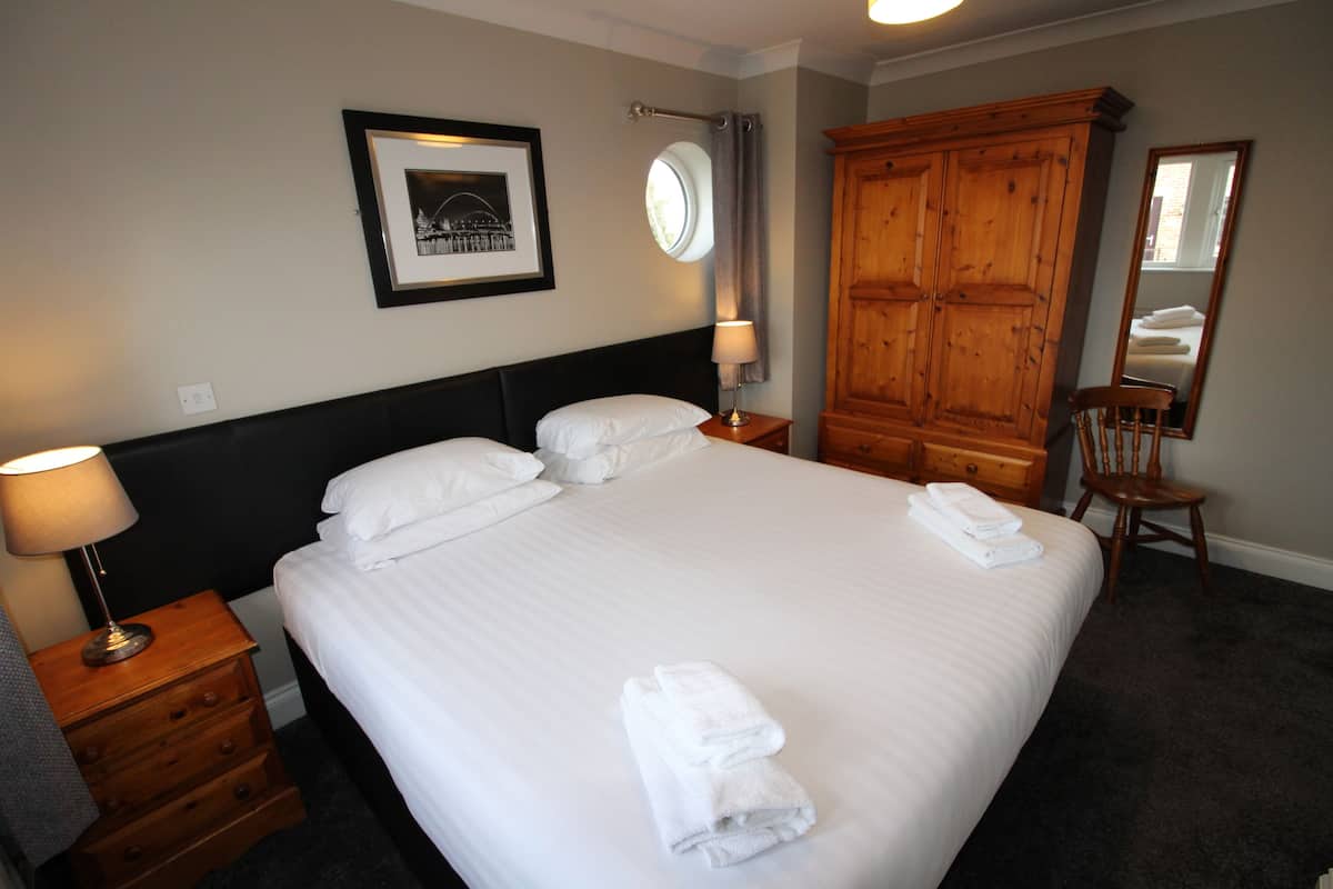 Une chambre d’hôtel avec un grand lit, une armoire en bois, un miroir et un tableau encadré au mur.