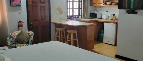 A compact bedroom with a bed, a small kitchenette, and a wooden ceiling.