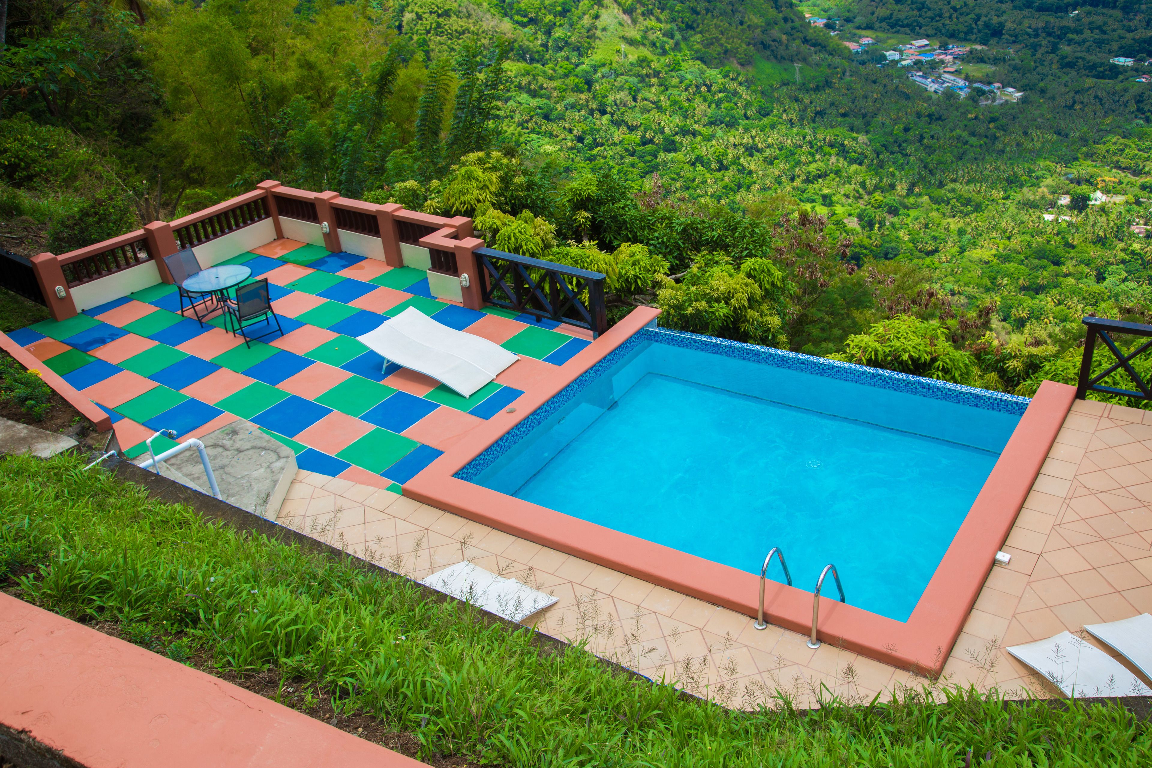 A swimming pool with a checkered deck, surrounded by a wooden deck and a view of a lush green landscape.