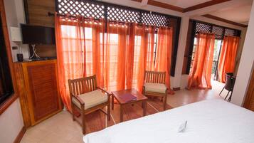 A hotel room with a bed, two wooden chairs, a small table, a TV, and orange curtains.