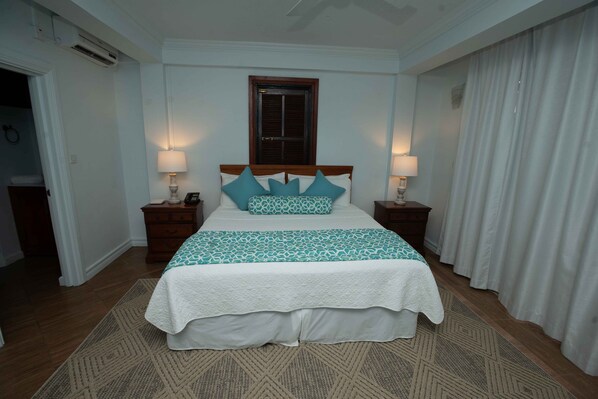 Une chambre à coucher bien rangée, avec un lit, deux tables de chevet et une fenêtre avec des volets.