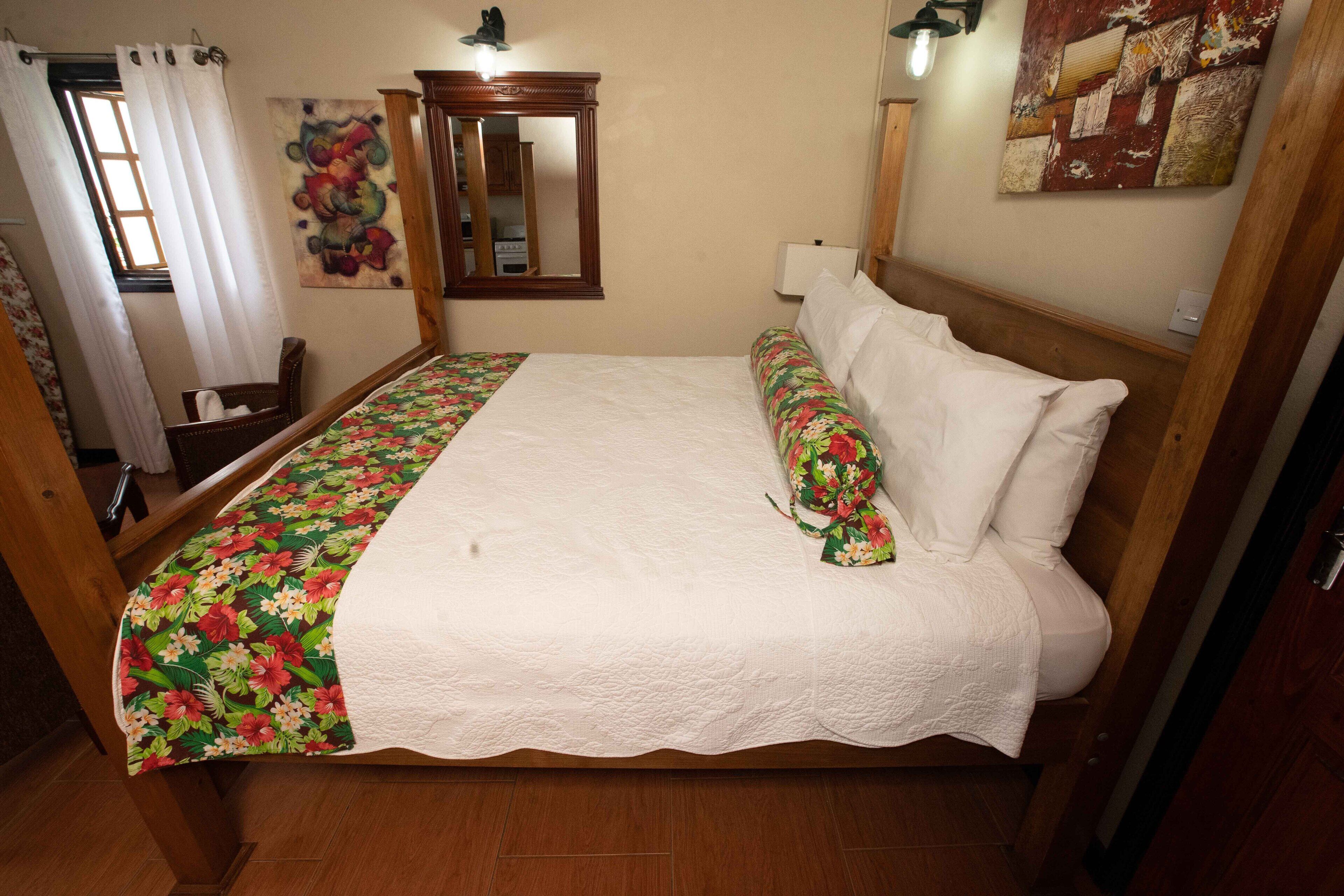 A neatly made bed with a floral bedspread, a wooden headboard, and a mirror above it.