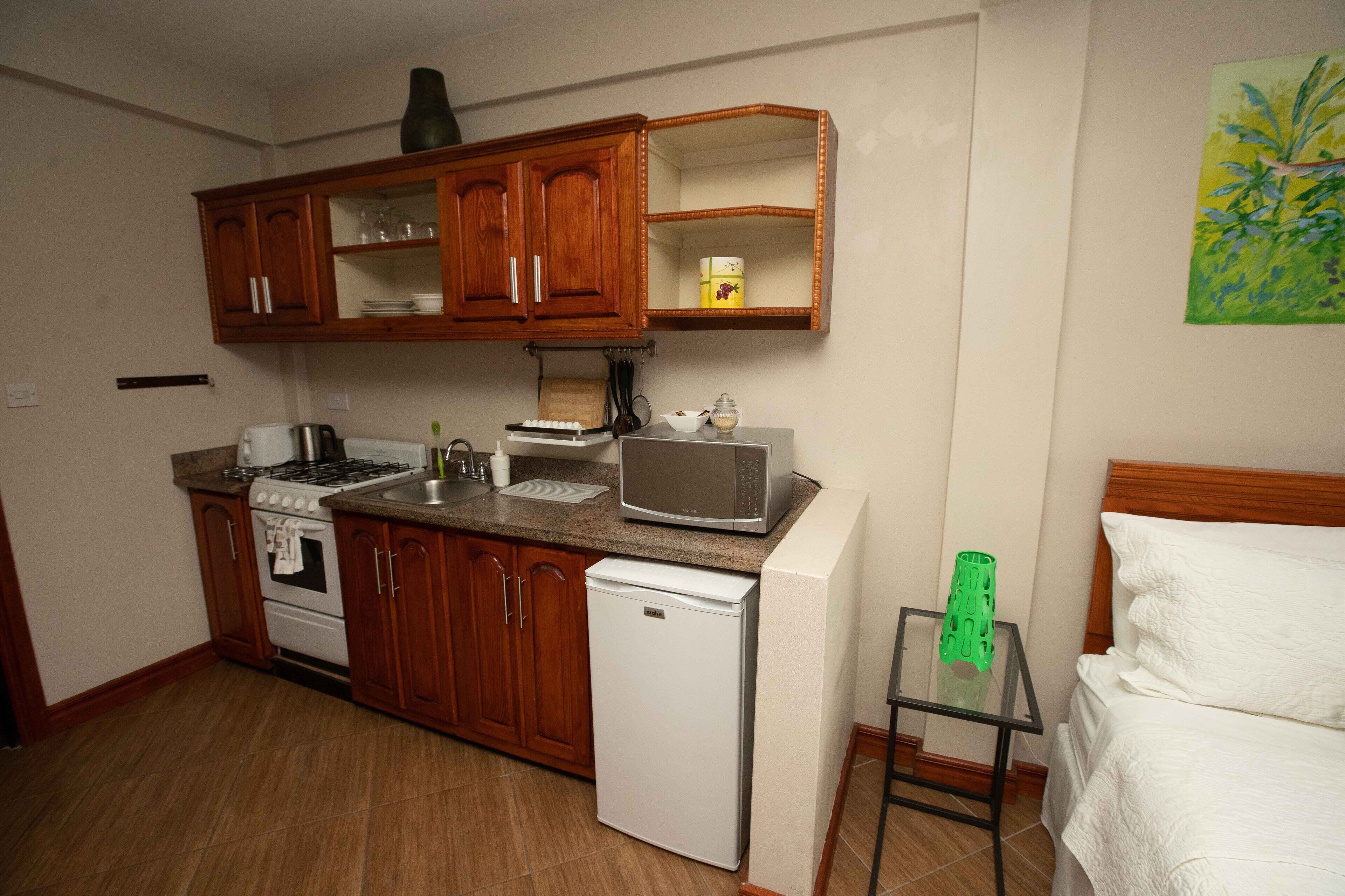 A compact kitchen with wooden cabinets, a microwave, a refrigerator, and a small table with a green vase.