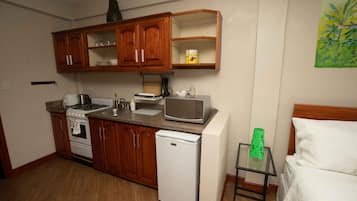 A compact kitchen with wooden cabinets, a microwave, a refrigerator, and a small table with a green vase.