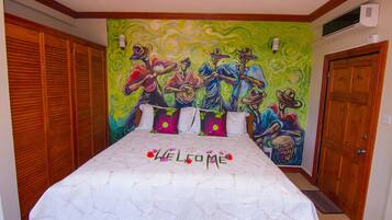 A bedroom with a bed, a colorful mural on the wall, and a wooden door.