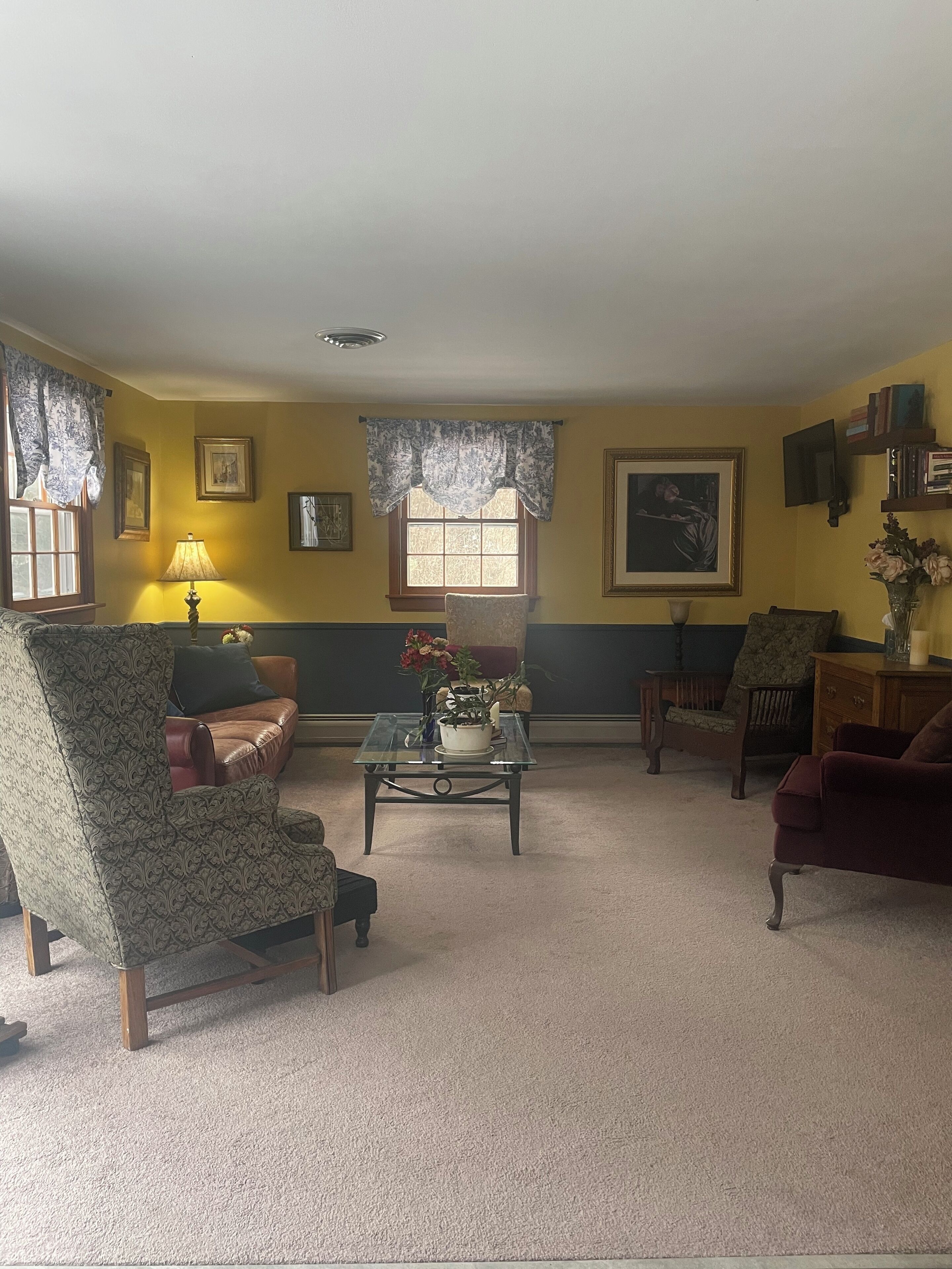 Uma sala de estar com uma poltrona estampada, um sofá, uma mesa de centro com um vaso de flores e uma estante de livros.