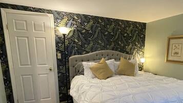 A bedroom with a bed, a door, a wall with a floral pattern, and a framed picture.