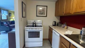 A compact kitchen with a stove, oven, and sink, wooden cabinets, and a red rug on the floor.