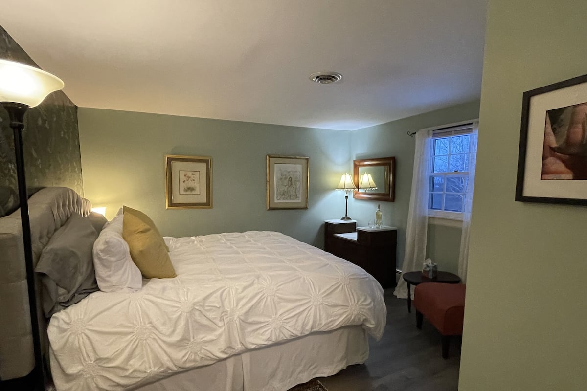 A neatly made bed with white bedding, a bedside table with a lamp, and two framed pictures on the wall.