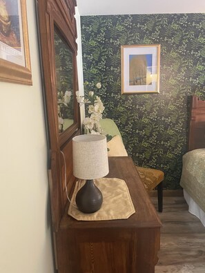 A wooden desk with a lamp, a framed picture, and a vase with white flowers.