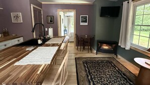 Una cocina moderna con encimera de madera, un lavamanos integrado y una chimenea. Hay una zona de comedor con mesa y sillas, y un televisor montado en la pared.