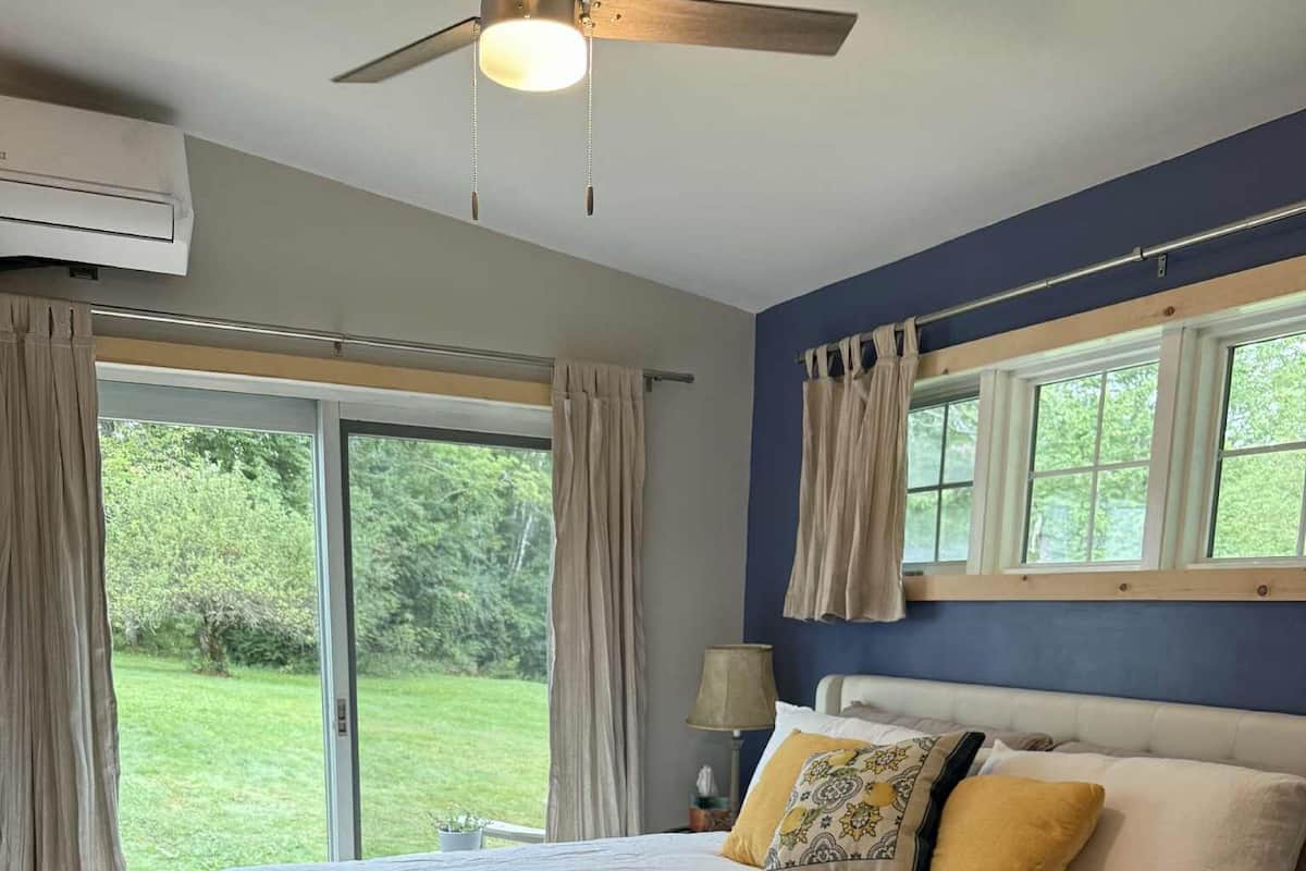 A bedroom with a large bed, a ceiling fan, and a view of the outdoors.