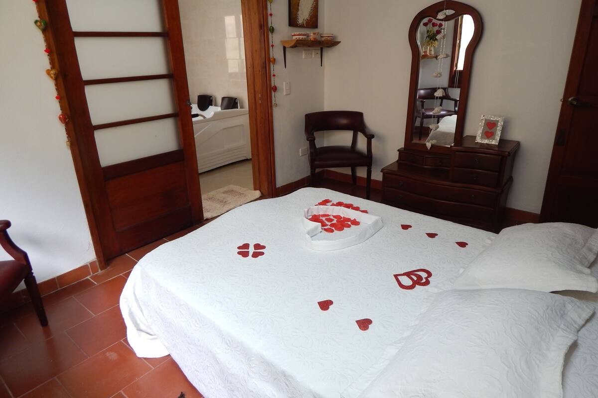 Un dormitorio con una cama, una silla de madera, un aparador y un espejo.
