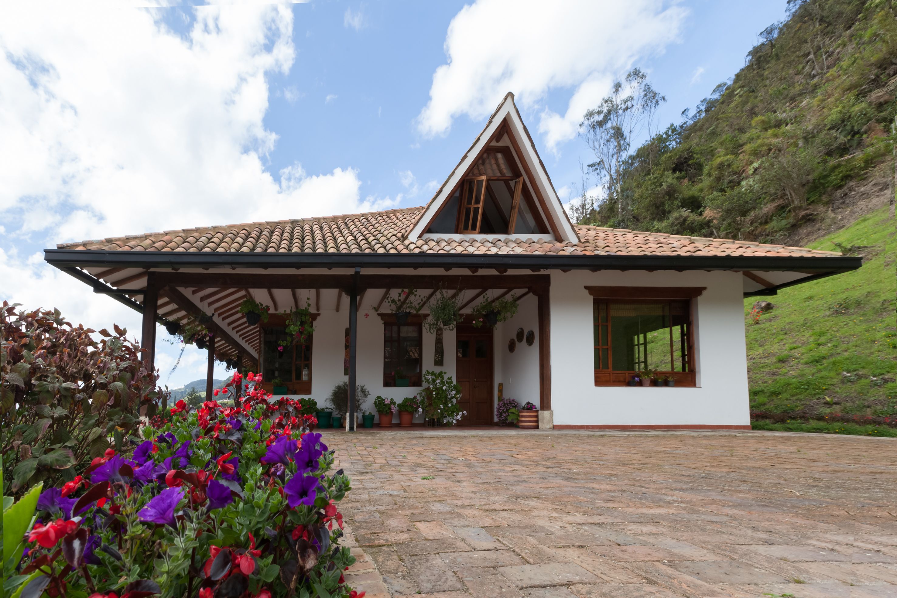 Ein Haus mit einem Ziegeldach, einer Veranda und einem Garten mit violetten und roten Blumen.
