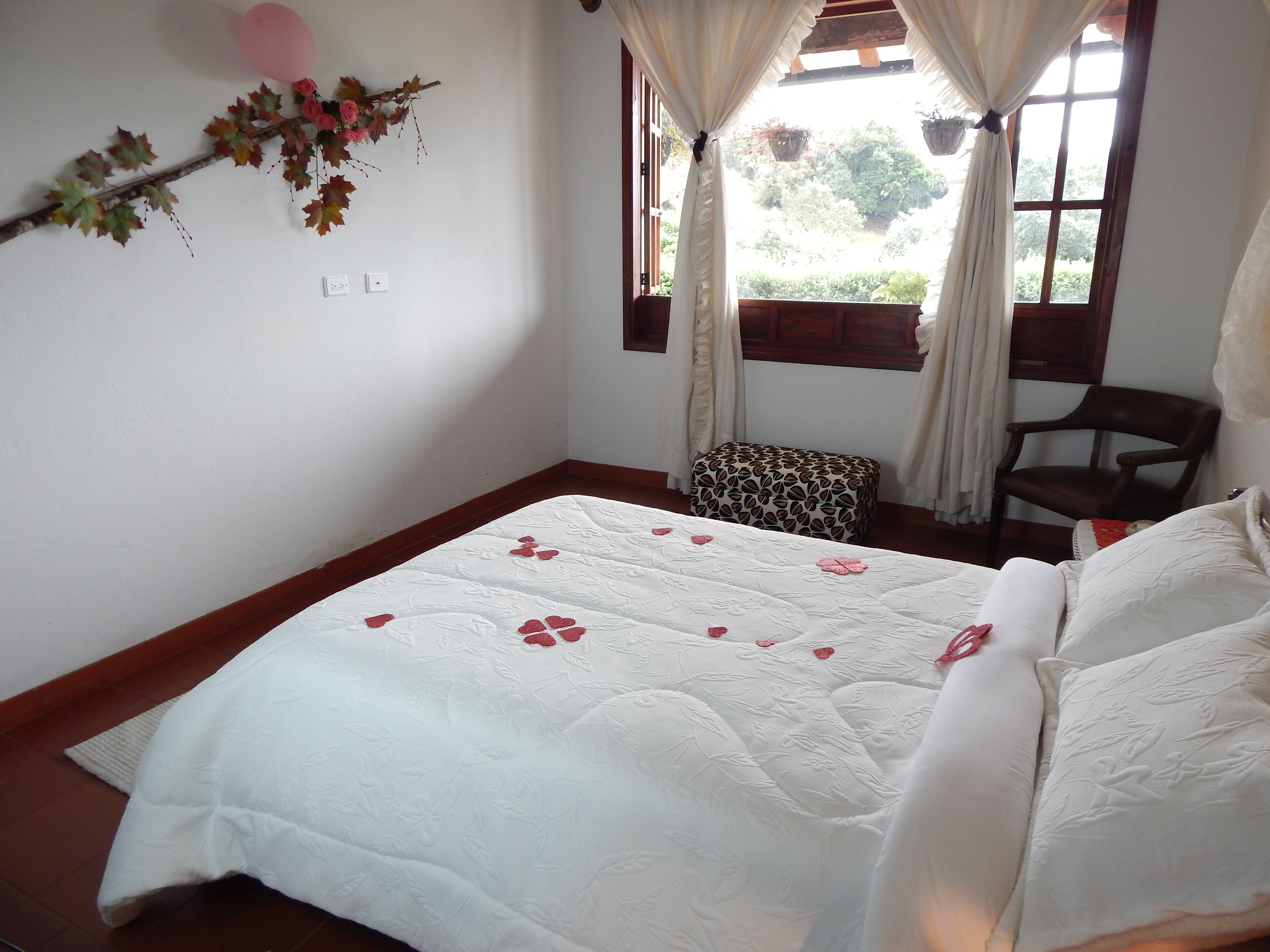Un dormitorio con cama, una silla, un ventanal con cortinas y un adorno en la pared.