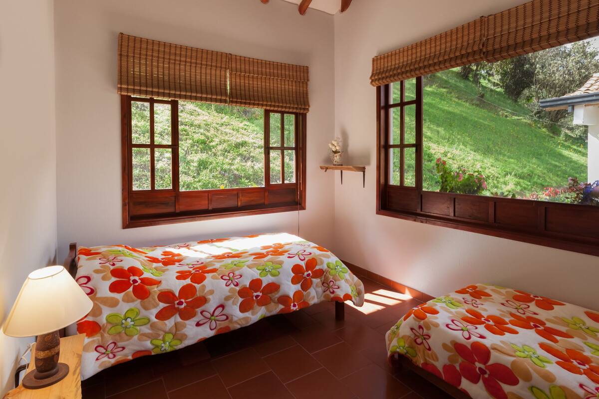 Un dormitorio con dos camas, una lámpara y una ventana con vistas a un jardín.