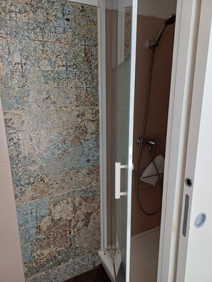 A bathroom with a shower, a glass door, and a patterned tile wall. - Hôtel de la Mer (Valras-Plage)