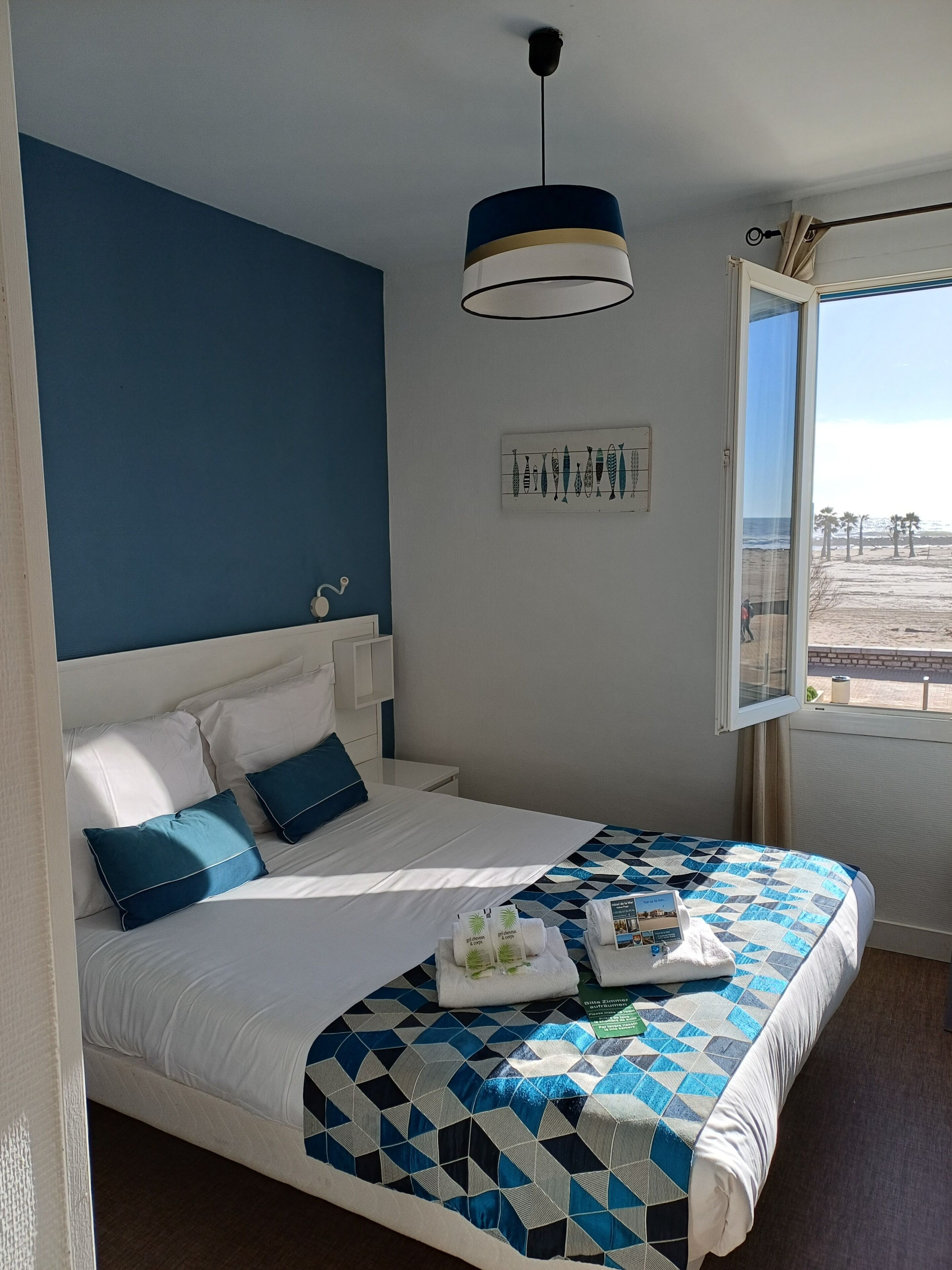 A bedroom with a bed, a window with a view, a hanging light fixture, and a wall-mounted artwork.