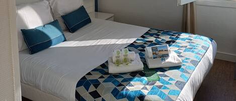 A bedroom with a bed, a window with a view, a hanging light fixture, and a wall-mounted artwork.