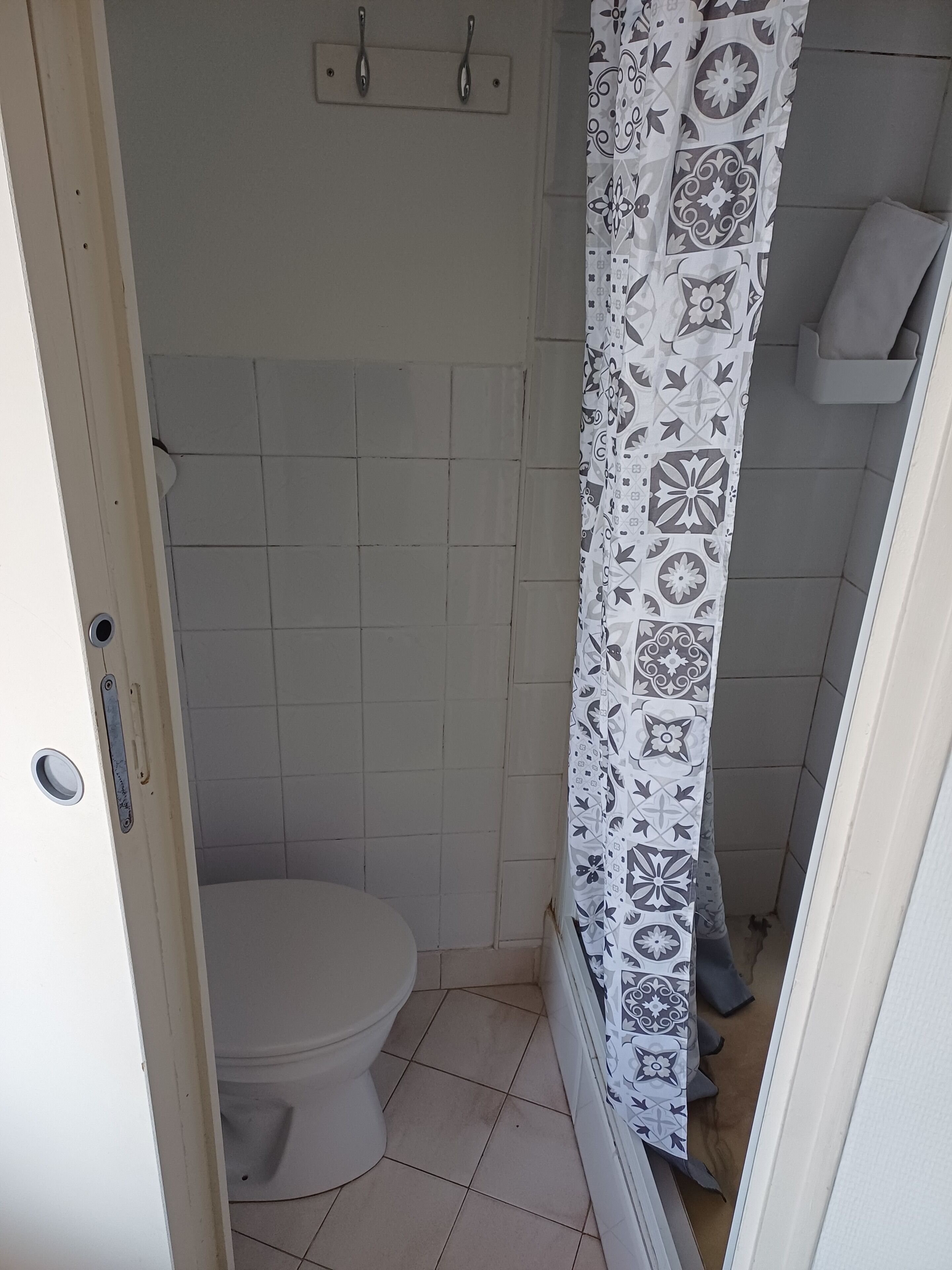 Un baño pequeño con inodoro, cortina de ducha estampada con un diseño geométrico y piso de baldosas.