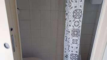 Une petite salle de bain avec des toilettes, un rideau de douche à motifs géométriques et un sol carrelé.