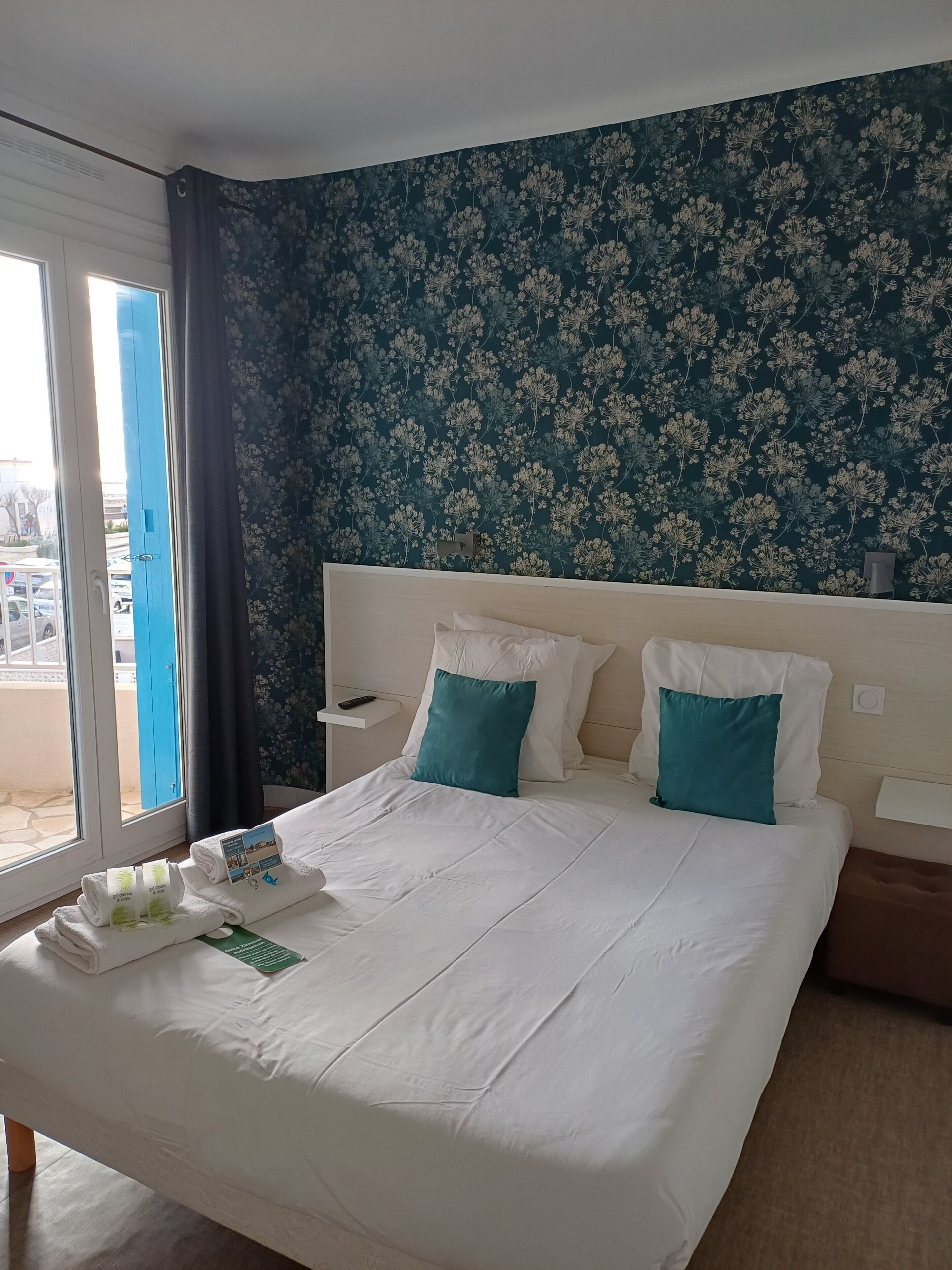 A hotel room with a bed, a nightstand, a window with curtains, and a view of the outside.