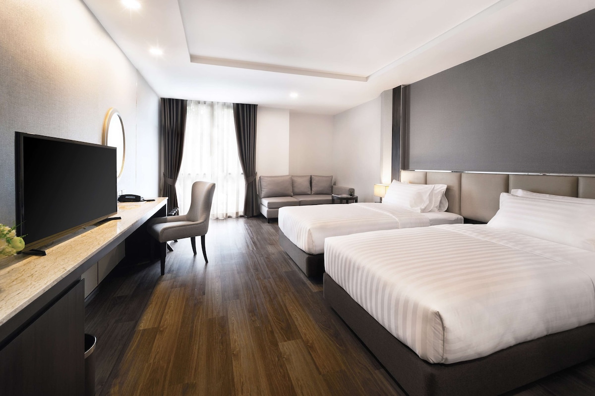 Una habitación de hotel moderna con dos camas, un escritorio, un televisor de pantalla plana, una silla y un sofá.