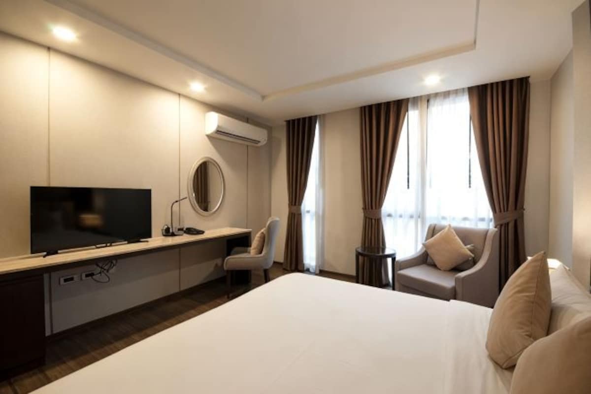 Una habitación de hotel con cama, escritorio con televisor, silla y una pequeña mesa.