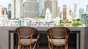 A cityscape view from a balcony with two wicker chairs and a black table. - SureStay Plus Hotel by Best Western Sukhumvit 2 (Bangkok)