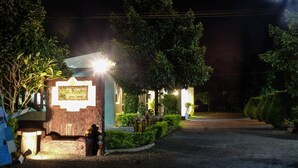 A well-lit entrance with a sign, surrounded by greenery and a paved path leading to the building. - Bai Pai Resort (Khlung)