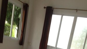 A neatly made bed with white linens and two pillows, a small bedside table with a pink object, and a window with curtains. - Bai Pai Resort (Khlung)