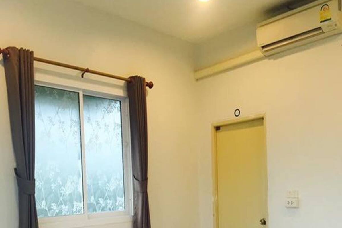 Un lit simple avec du linge de lit blanc, une fenêtre avec des rideaux, un appareil de climatisation et une porte.