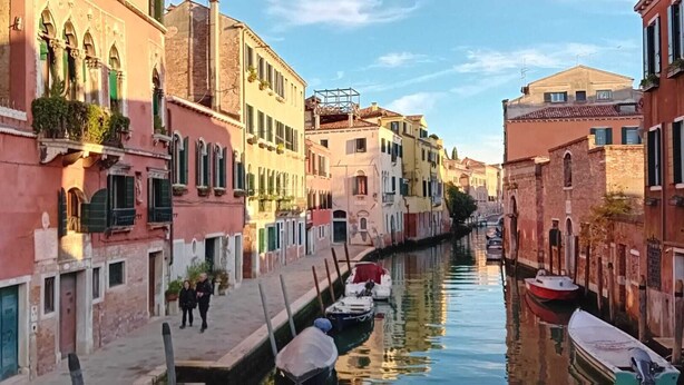 A narrow canal flanked by historic buildings with balconies and windows, a pedestrian walkway, and boats docked along the water. - A quiet corner in the "True Venice" (venezia)