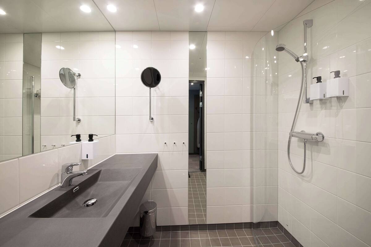 A modern bathroom with a large mirror, a sink, a shower, and a toilet.