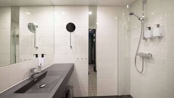 A modern bathroom with a large mirror, a sink, a shower, and a toilet.
