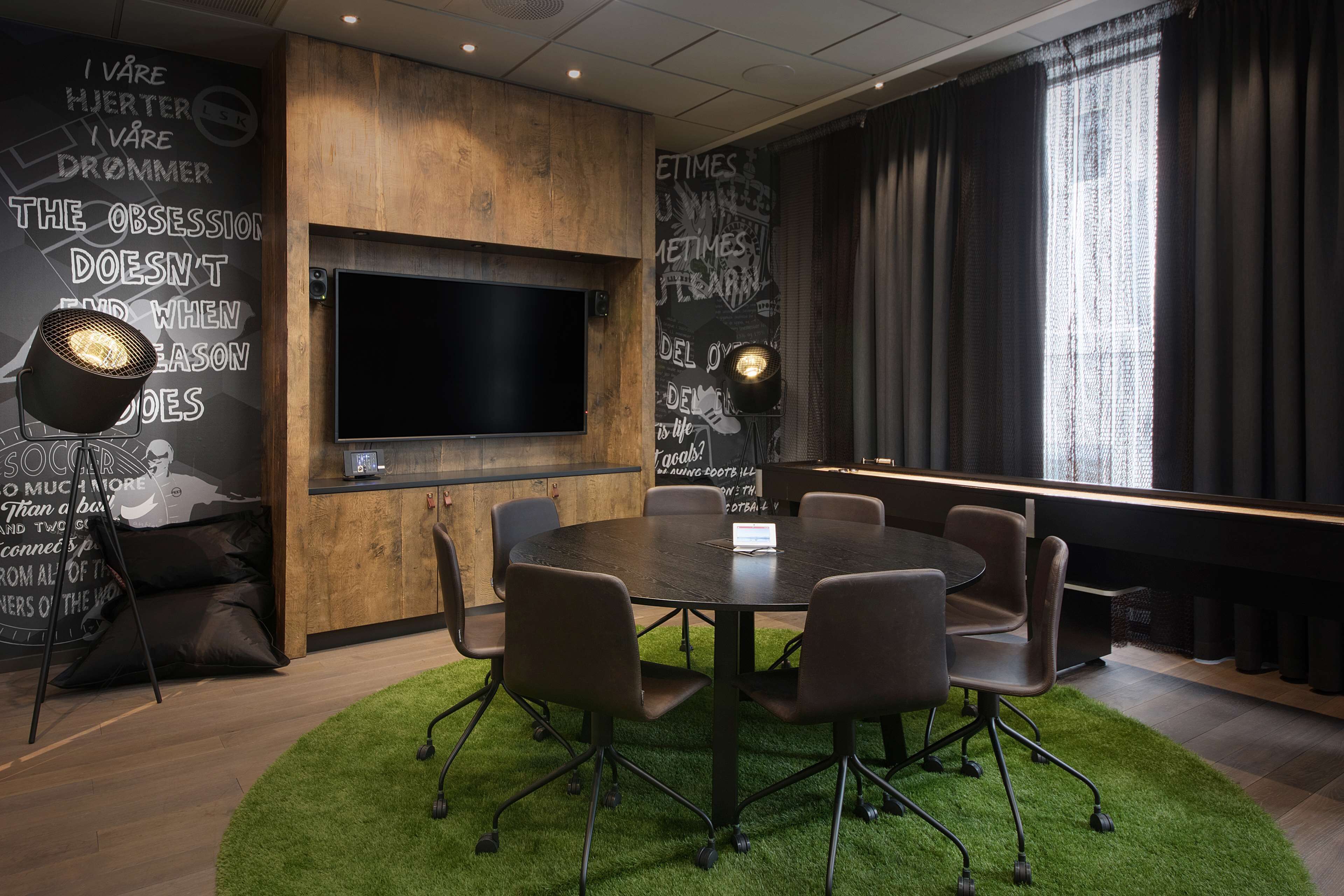 Un salón de conferencias con una gran mesa, sillas, un televisor y una pared con citas motivacionales.