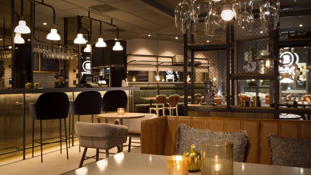 L’intérieur d’un restaurant avec un bar, des sièges agrémentés de coussins et des luminaires suspendus.