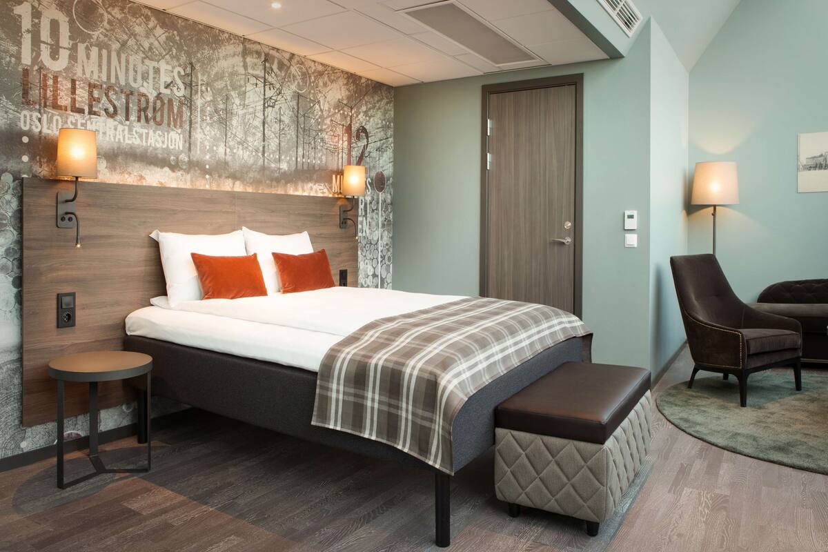 A modern hotel room with a large bed, a bench, a chair, and a wall with a cityscape mural.
