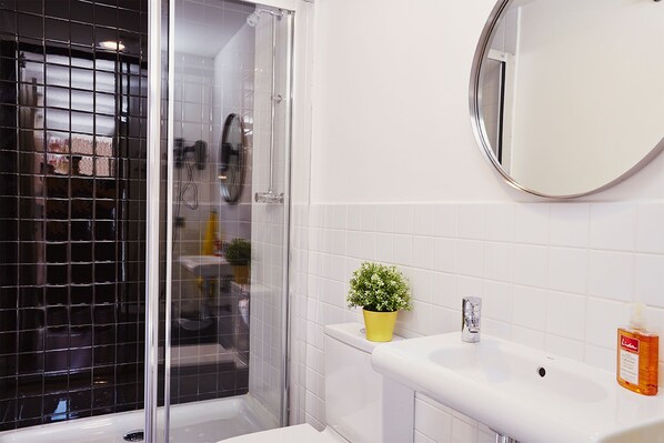 Un baño con cabina de ducha de vidrio, un lavamanos blanco, una planta en maceta y un espejo redondo.