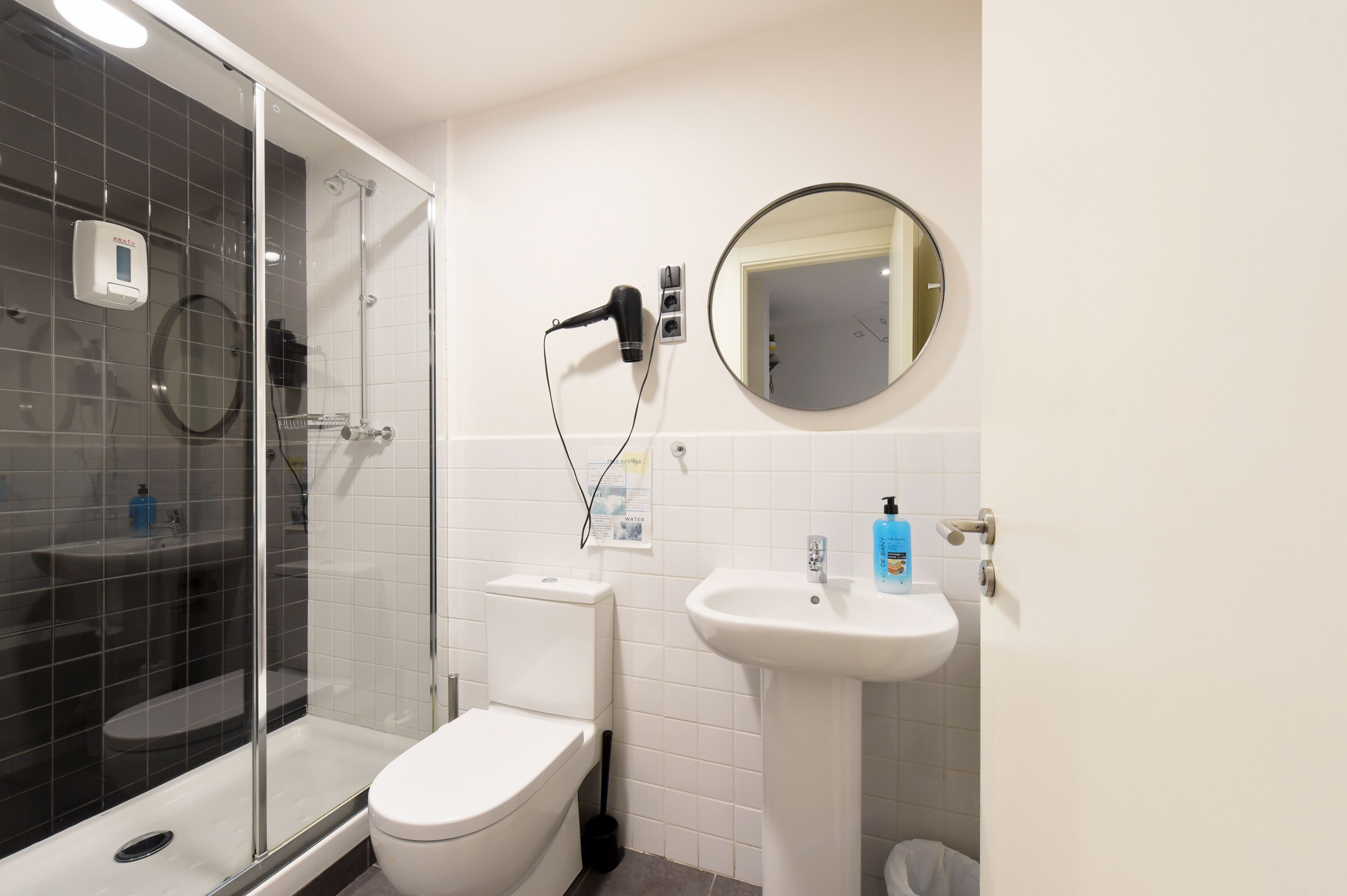 A modern bathroom with a glass-enclosed shower, a toilet, a sink, and a hairdryer on a wall-mounted station.